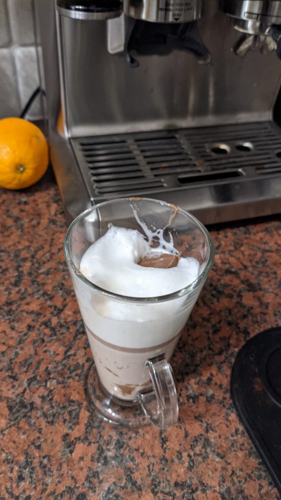 Poorly made hot chocolate with chocolate square fallen into the foam of the milk